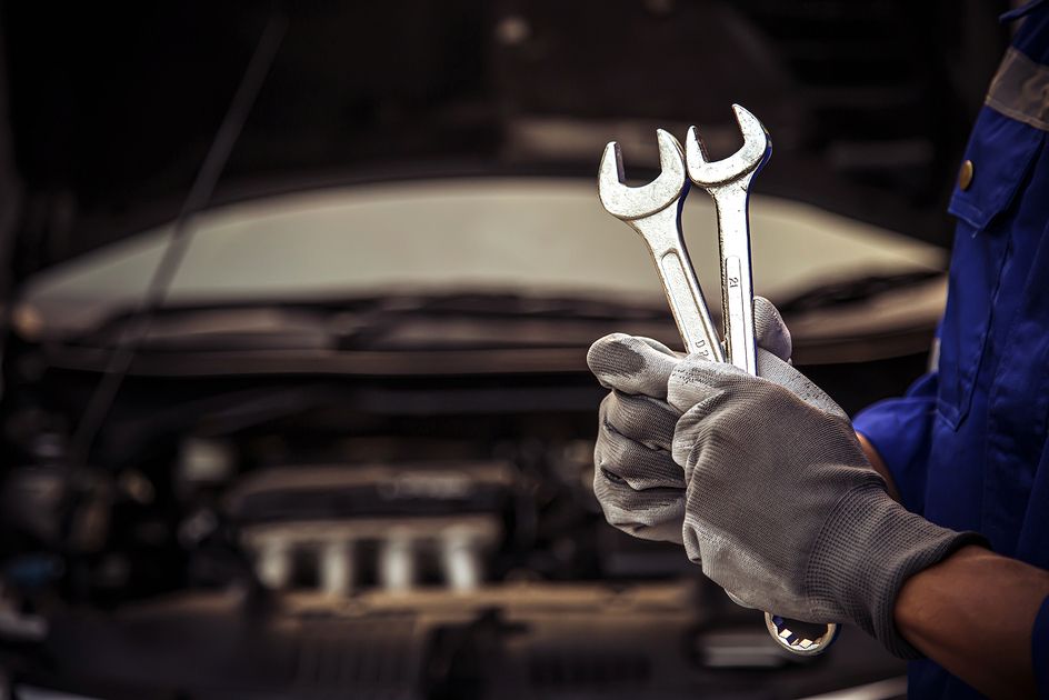 Eine Person hält zwei Schraubenschlüssel vor einem zu reparierenden Fahrzeug